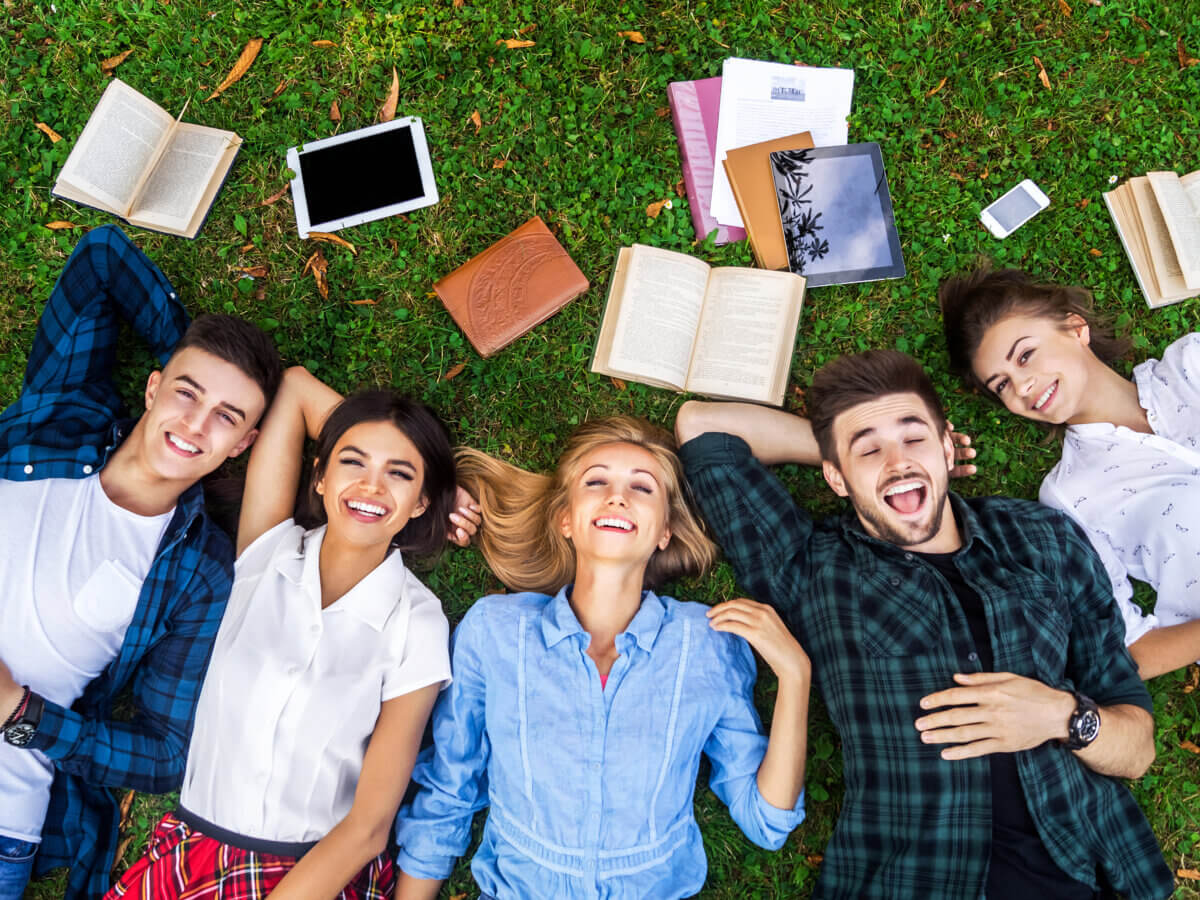 Students lying on their backs on the grass with books lying around.