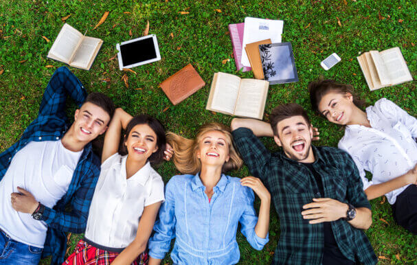 Students lying on their backs on the grass with books lying around.