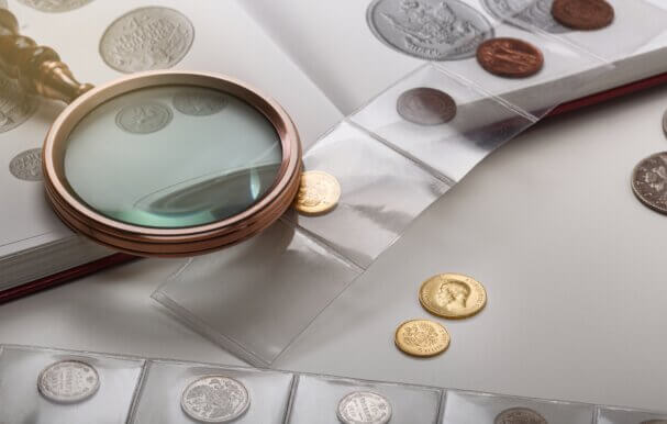 Antique collectable coins on a table with a book and a magnifying glass.