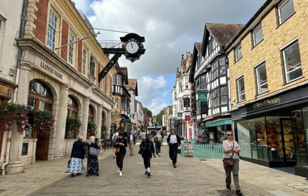 An image of winchester town centre with people walking through the centre and shops surrounding them.