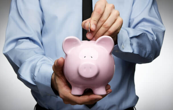 An image of a business man putting a coin into a pink piggy bank.