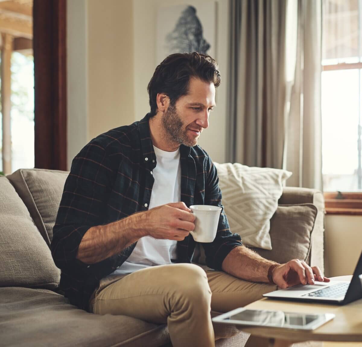 A man sitting on the sofa, with a cup of tea in his hand as he works from home in Swindon.