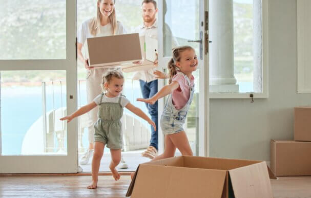 An image of a family moving into their new home in Newbury with two parents holding boxes and two children running through the door.