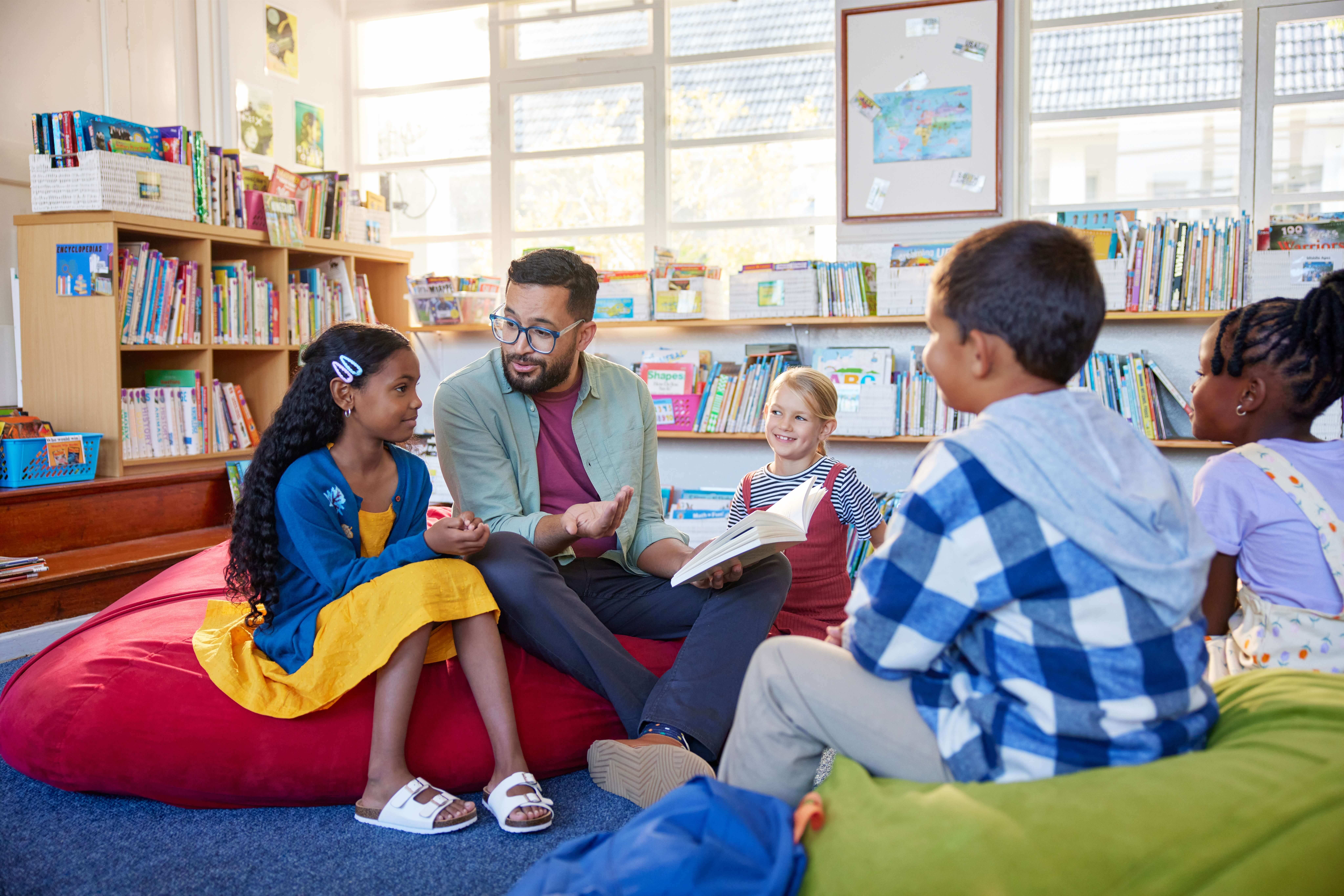 An image of a group of school children in a classroom in Lydney, sitting on bvean bags and being read to by a teacher.